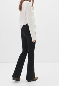 Jean noir évasé taille haute avec deux poches arrière, associé à un haut blanc à manches longues ample et des bottines.