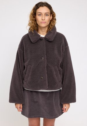 Dunkelgraue, flauschige Lammfelljacke mit Kragen, großen Taschen und Knöpfen, kombiniert mit einem passenden Cordrock. Minimale Texturdetails.
