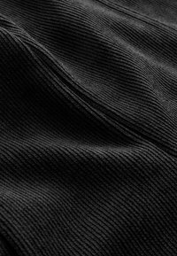 Close-up van zwart ribbelstof met zichtbare naad en textuur van parallelle lijnen die zachte plooien creëren.