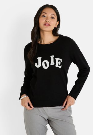 Pull en tricot noir avec le lettrage blanc "Joie", col rond, manches longues et ourlet ajusté. Détails texturés sur les lettres.