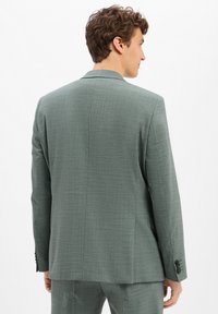 Herrenanzugjacke aus leicht grünem Stoff mit strukturiertem Muster, mit einem Schitz am Rücken und schwarzen Knopfakzenten an den Manschetten.