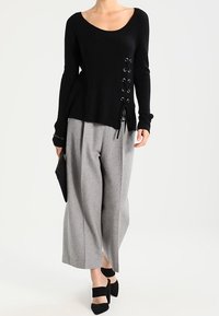 Musta ribbineule, jossa nyöritys sivussa, yhdistetty harmaisiin leveälahkeisiin housuihin ja mustiin korkokenkiin. Kädessä musta clutch-laukku.