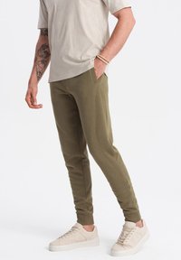 Olijfgroene tapered joggingbroeken van een zachte katoenmix, met zijzakken en geribbelde boorden, gecombineerd met lichtbeige sneakers.