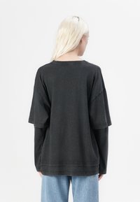 Zwarte oversized T-shirt met korte mouwen, losse pasvorm en een ronde halslijn. Zachte katoenen stof met zichtbare stikseldetails.