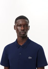Námořnická polo košile vyrobená z texturované tkaniny, s klasickým límcem, dvěma knoflíky a vyšitým logo aligátora na levé části hrudi.