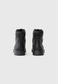 Botas de cuero negro hasta el tobillo con una superficie texturizada, forro de piel sintética en la parte superior y suelas de goma robustas diseñadas para condiciones invernales.