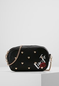 Musta tikattu käsilaukku, jossa on kultaiset sydänkoristeet ja ketjuhihna. Ominaisuuksina brändin logo ja huulikuva yhdellä sivulla.