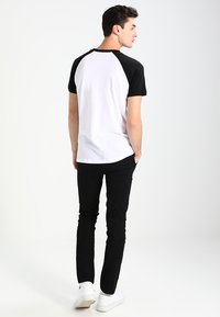 Camiseta raglán en blanco y negro con mangas cortas, que presenta un cuerpo blanco y mangas negras. Diseño sencillo, material de algodón y corte casual.