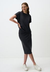 Zwarte T-shirt met bijpassende midi-rok, gemaakt van gladde stof; heeft een relaxed fit en korte mouwen. Draagt een paar witte sneakers.