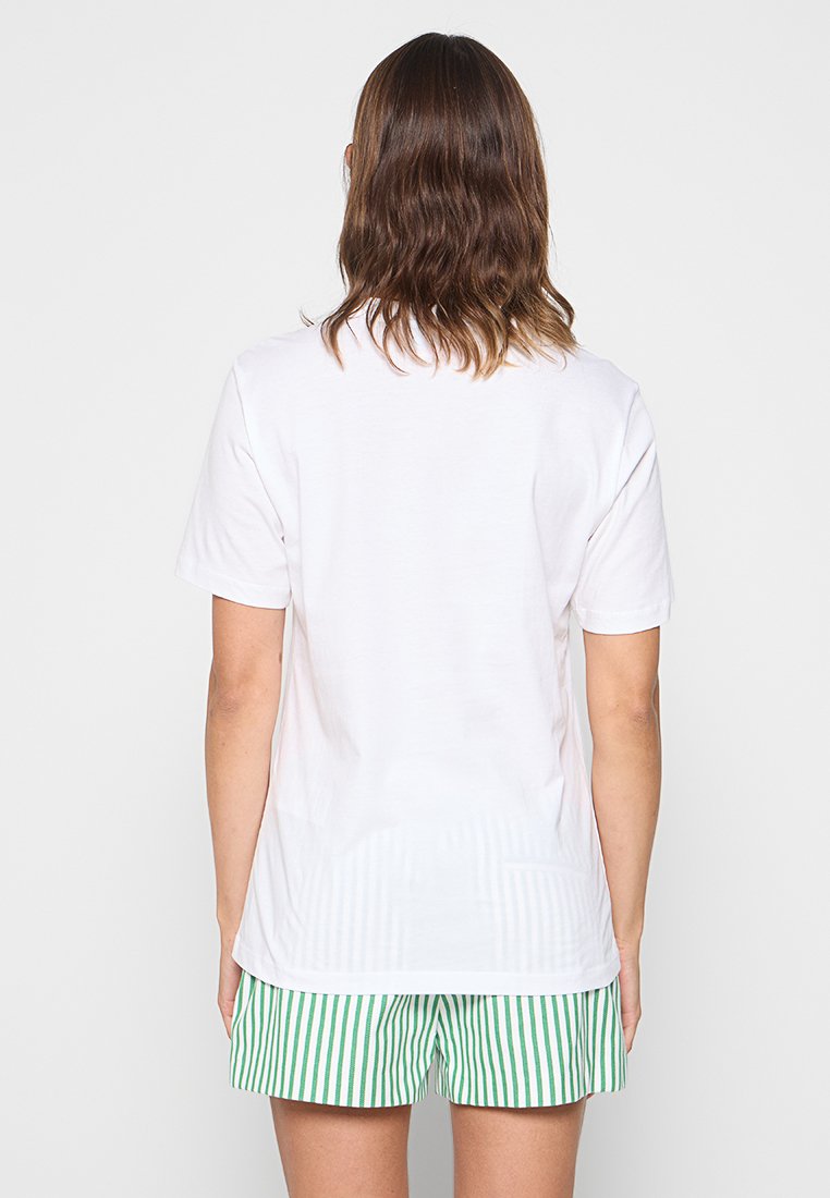 T-shirt blanc à manches courtes avec une coupe décontractée, vu de l'arrière. Doté d'une texture lisse et d'un ourlet droit. Associé à un short rayé vert et blanc.