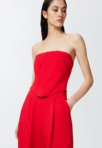 Monos de tirantes rojos sin mangas con un cuerpo ajustado y piernas anchas, que presenta una construcción sin costuras y bolsillos. Tejido suave con un acabado mate.