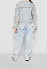 Farkkutakki vaaleansinisellä shearling-kauluksella, yhdistettynä vaaleansinisiksi happovärjättyihin löysiin farkkuihin, esiteltynä takaa.