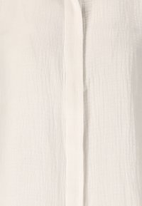 Witte linnen blouse met een gestructureerd oppervlak, met een verticale sluiting en subtiele plooien. Lichtgewicht en ademend stof.