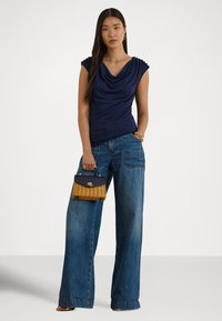 Granatowa bluzka z golfem i marszczonymi ramionami, zestawiona z szerokimi, jasnoniebieskimi dżinsami. Dodatkiem jest mała pleciona torebka.