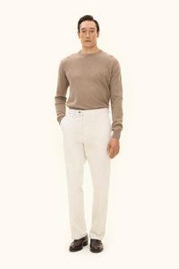 Beiger Pullover, cremefarbene Hose, braune Schuhe. Einfaches Design, taillierte Silhouette, weicher Stoff und ein Knopfdetail an der Hose.