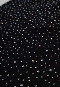 Czarna tkanina ozdobiona licznymi błyszczącymi cyrkoniami w różnych rozmiarach, tworzącymi rozproszony wzór na powierzchni.