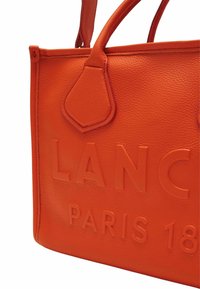 Narancssárga bőr válltáska textúrázott felülettel, az elején dombornyomott "LANC" és "PARIS 18" felirattal, lekerekített fogantyúkkal.