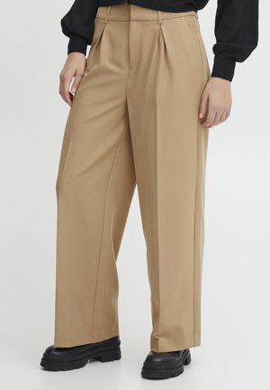 Beige wide-leg trousers with front pleats, smooth fabric, and a high waist, paired with black chunky-soled shoes.