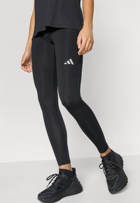 Mallas negras hechas de tela elástica, con un logo reflectante de Adidas, ajuste ceñido y costuras cosidas para un diseño elegante. Combínalas con zapatillas negras.