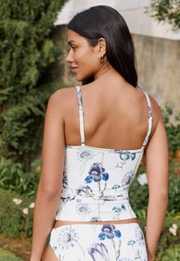 Bikini-Oberteil mit Floralprint und dünnen Trägern, das ein enges Design und einen gerafften Textur in Weiß-, Blau- und lila Farbtönen aufweist.