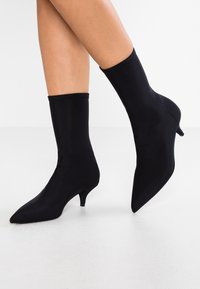 Černé elastické kotníkové boty s špičatou špičkou a štíhlým podpatkem, s hladkým, přiléhavým designem, který objímá kotník.