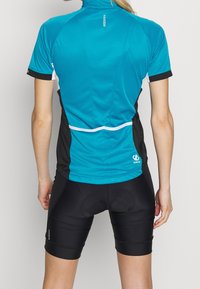 Cyklistický dres s krátkým rukávem v tyrkysové a černé barvě, s rolovacím zipem, texturovanou tkaninou a reflexními detaily. Kombinován s černými polstrovanými kraťasy.