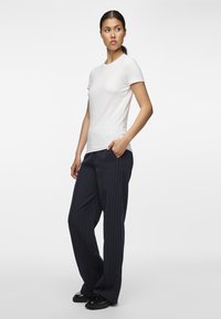 Valge lühikeste varrukatega T-särk, mis on kombineeritud tume laevavärvi peenetriibuliste laiade pükstega. Pükstel on küljetaskud ja need istuvad vabalt. Mustad jalanõud lisavad välimusele viimase lihvi.