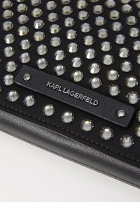 Black clutch featuring a studded design with clear, faceted rhinestones and a textured black leather label embossed with "KARL LAGERFELD."