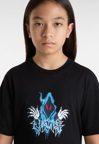 Camiseta negra de algodón con un diseño gráfico de una figura en capucha azul con ojos rojos y manos blancas, acentuada por texto estilizado.