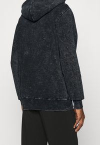 Mikina s kapucí v tmavě šedé barvě z měkké, strukturované tkaniny. Disponuje volným střihem a vroubkovanými manžetami na rukávech a spodním lemu.