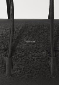 Sac à main en cuir noir avec une finition texturée, doté de longues anses élégantes et d'un logo argenté embouti à l'avant.
