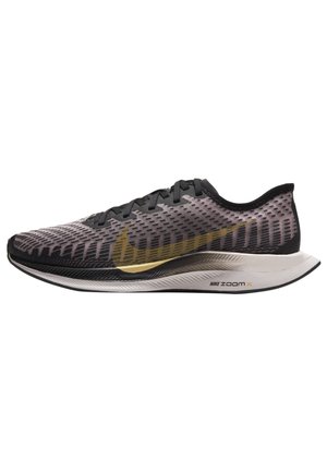 Czarny i szary but do biegania Nike ZoomX z złotym logo Swoosh i białą podeszwą, widok z boku na białym tle.