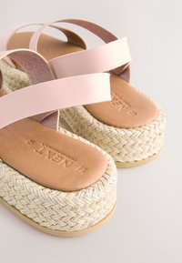 Sandales à brides en cuir rose avec une plateforme en jute tissée et une semelle intérieure en cuir lisse couleur tan, avec une finition texturée sur les brides.