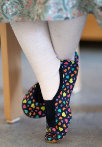 Kleurrijke slip-on schoenen met hartpatroon in marineblauw met zwarte accenten, gecombineerd met lichtgekleurde panty’s, getoond terwijl gezeten.