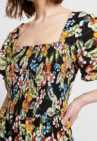 Kwiatowa sukienka z kwadratowym dekoltem, krótkimi bufkami i marszczonym gorsetem. Czarne tło z żywymi wzorami w kolorze czerwonym, niebieskim i zielonym.