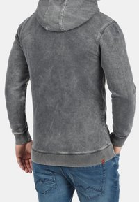 Grijze hoodie met een gestructureerde afwerking, voorzien van een capuchon met trekkoord en geribde manchetten en zoom. Gecombineerd met blauwe spijkerbroek.