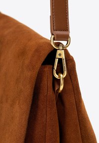 Brązowa zamszowa torba z rogami, prezentująca zapięcie z metalowej złotej okładki oraz skórzany pasek. Tekstura jest miękka, z widocznymi detalami szycia na krawędzi.