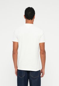 Λευκό κοντομάνικο T-shirt με στρογγυλή λαιμόκοψη και διακριτική ραφή V στο πίσω μέρος, φτιαγμένο από μαλακό βαμβακερό ύφασμα. Φορεμένο με σκούρα τζιν.