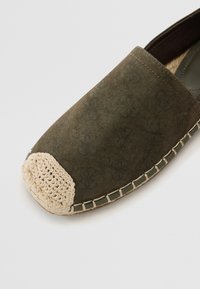 Espadrille-jalkine tummanoliivinvihreästä kankaasta, jossa on kuvioitu muotoilu, luonnollinen juuttikärki ja kontrastiväriset tikit pohjassa.