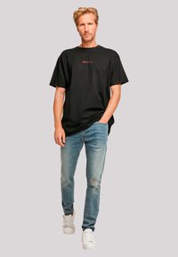 Zwarte katoenen t-shirt met ronde hals, met daarop in het rood Japans tekst. Gedragen met lichtblauwe ripped jeans en witte sneakers.