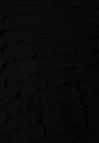 Svart stickad tyg med en ruffled textur, med lager av horisontella ränder som skapar visuell djup och ett mjukt utseende.