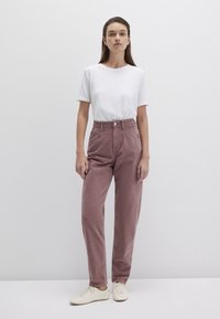 Weißes Baumwoll-T-Shirt, hochgeschnittene rosa Cordhosen, gerade Passform, mit Fronttaschen und minimalistischen weißen Sneakers.