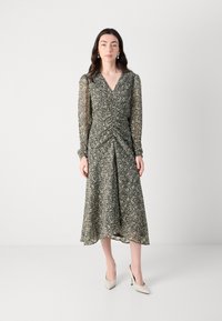 Robe portefeuille florale avec de longues manches transparentes, encolure en V, taille froncée et ourlet fluide. Couleurs : noir, crème et motifs vert olive.