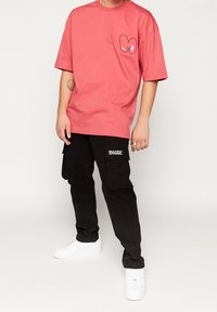 Camiseta rosa de manga corta con cuello redondo y un gráfico negro en el pecho, combinada con pantalones cargo negros y zapatillas blancas.