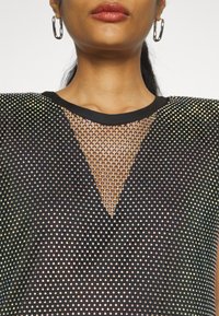 Černý top s síťovinovým designem, který má třpytivé, reflexní akcenty, výstřih do V a solidní černý límeček.