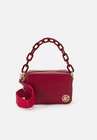 Sac à main texturé rouge avec un logo doré, doté d'une poignée en chaîne et d'une bandoulière en tissu amovible. Fermeture zippée et forme rectangulaire.