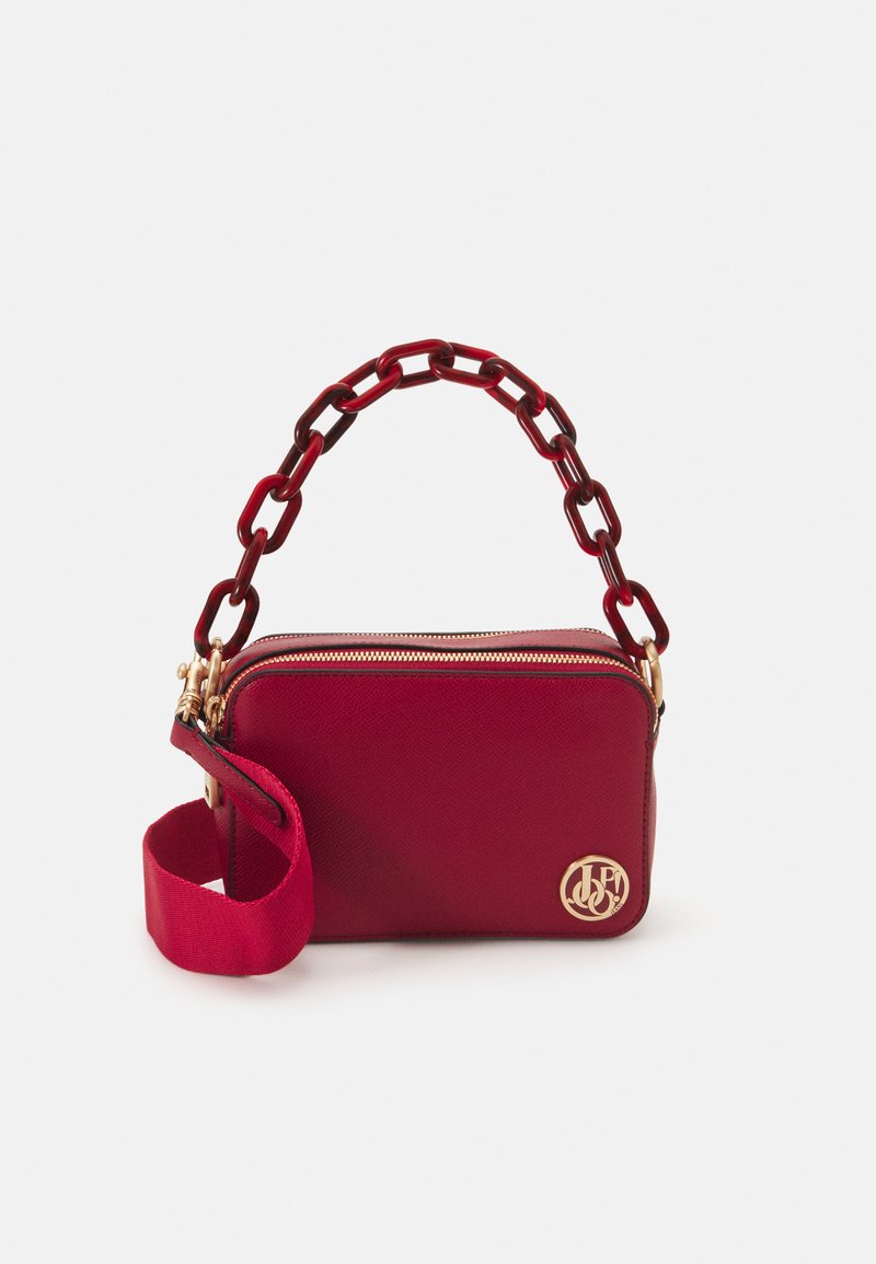 Sac à main texturé rouge avec un logo doré, doté d'une poignée en chaîne et d'une bandoulière en tissu amovible. Fermeture zippée et forme rectangulaire.