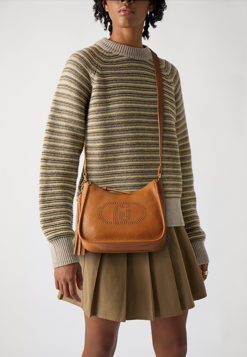 Borsa a tracolla in pelle arancione con logo perforato, abbinata a un maglione a righe e a una gonna plissettata, creando un design di outfit a strati.