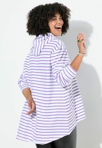 Sudadera con capucha a rayas blancas y moradas, de manga larga, ajuste relajado y dobladillo asimétrico, combinada con leggings negros. Sin elementos metálicos destacados.