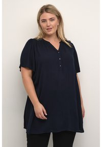 Tunic blu navy a maniche corte con scollatura a V, dotata di bottoni e tessuto texture, abbinata a pantaloni neri.